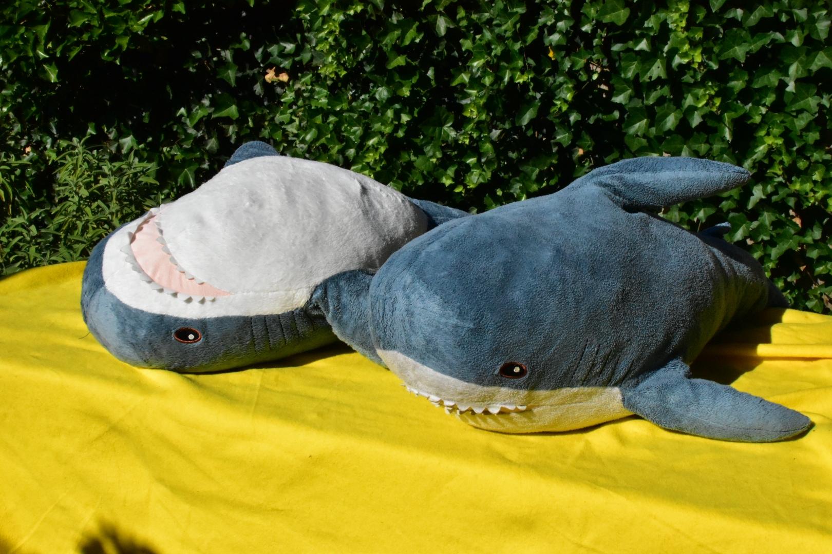 Two Blåhaj cuddly sharks lying outside on a table on a yellow blanket. One is lying on their back and one on their belly.

Don't get a sunburn!